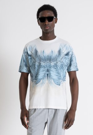 Camiseta blanca de manga corta con un estampado de hoja de palma azul, hecha de una tela suave, combinada con pantalones grises texturizados y gafas de sol negras.