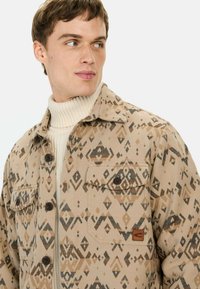 Tan gekleed jasje met een ruitpatroon in bruin en zwart. Voorzien van bruine knopen en een borstzak.