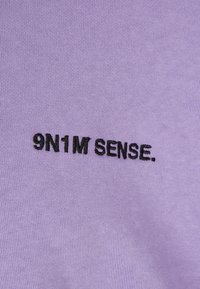 Levendula színű pamut póló, fekete hímzett "9N1M SENSE." felirattal az elején. Sima tapintású és normál szabású kialakítás.