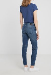 Tmavě modré tričko v kombinaci s úzkými, zesvětlenými modrými džíny s texturovaným povrchem a zadními kapsami. Doplněno bílými teniskami.