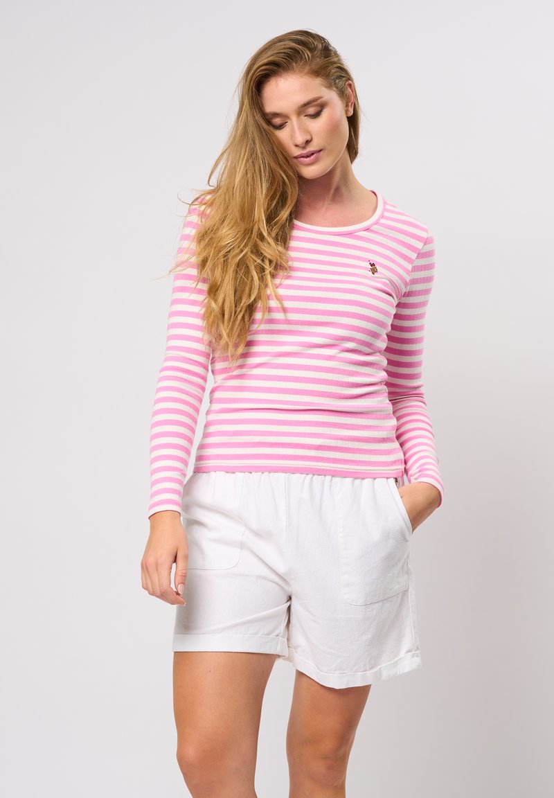 Pika ja valge triibuline pika varrukaga pluus ümmarguse kaelusega ja tikitud logoga, koos meeldivate valgete lühikeste pükstega, millel on taskud.