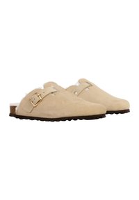 Zuecos de ante beige con un suave forro blanco, un acento de hebilla dorada, punta redondeada y suela de goma texturizada.