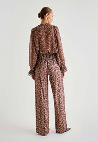 Musterbluse und weite Hose in Lila und Braun. Transparenter Stoff mit elastischem Bund, Puffärmeln und komplexem geometrischen Design.