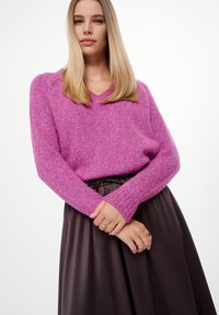 Roze, gestructureerde gebreide trui met een V-hals en lange mouwen, gecombineerd met een donkere, zijden rok die bij de taille is verzameld.