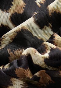 Tissu texturé en noir, beige et marron avec un motif léopard ; matériau en maille léger avec un tombé doux et une apparence froissée.