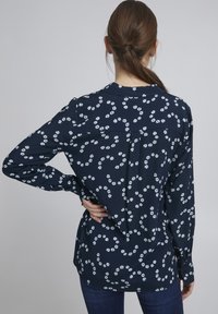 Navy blouse met lange mouwen, voorzien van een bloemenprint in lichtblauw, gemaakt van zachte stof met een rugplooidetail en knoopmanschetten.