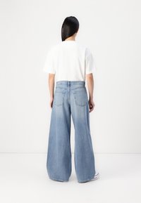 Jeans in denim a gamba larga di colore blu chiaro, con vita alta, tasche posteriori e una vestibilità rilassata. Abbinati a una t-shirt bianca basic.