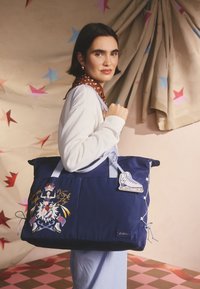 Didelė tamsiai mėlyna rankinė su mėlynomis detalėmis, dekoruota siuvinėtu dizainu ir ledo riedučių pakabuku. Pagaminta iš patvarios medžiagos.