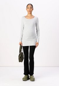 Langärmliges graues Oberteil, schwarze weit ausgestellte Hosen, grüne Clogs und eine olivfarbene Handtasche. Glattes Material mit taillierter Passform und Rundhalsausschnitt.