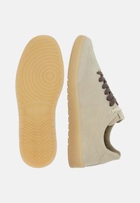 Beige suede sneakers with brown laces, featuring a smooth texture, round toe, and patterned rubber sole. Side perforations for ventilation.