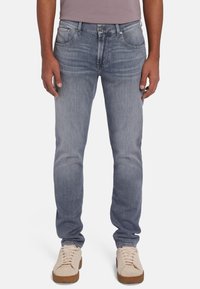 Lichtblauwe denim jeans met een rechte pasvorm, voorzien van vijf zakken en een subtiele vervaagde print. Gepaard met beige sneakers met platte veters.
