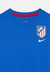 T-shirt blu con colletto interno rosso, caratterizzata dal logo del club Atlético Madrid e dallo swoosh bianco di Nike sul petto.