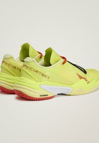 Een paar neongele sneakers met rode veters, gestructureerde zijkanten, rode zolen en merktekst op de hiel en de zijkanten van de zool.