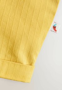 Gult ribstrikket stof med foldet kant og lille hvid label, der viser en rød chili med en blå hat.