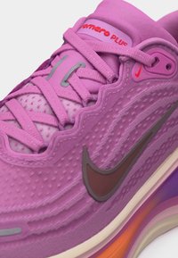 Zapatilla Nike Air Max rosa con parte superior texturizada ondulada, logo Swoosh oscuro, cordones rosas y suela visible con amortiguación de aire en colores naranja y púrpura.