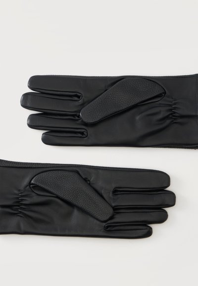 Ζευγάρι μαύρα δερμάτινα γάντια με υφασμένα patches για κράτημα στις παλάμες, τοποθετημένα επίπεδα σε λευκό φόντο.