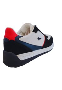 Sneaker neri, bianchi e rossi con una tomaia in tessuto effetto texture, dettagli blu, suola in gomma e un piccolo logo di un cane sul lato.