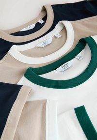 Trois t-shirts empilés ; le dessus est bleu marine avec un col crème, le milieu est beige avec un col blanc, le dessous est blanc avec un col vert. Tissu en coton doux.