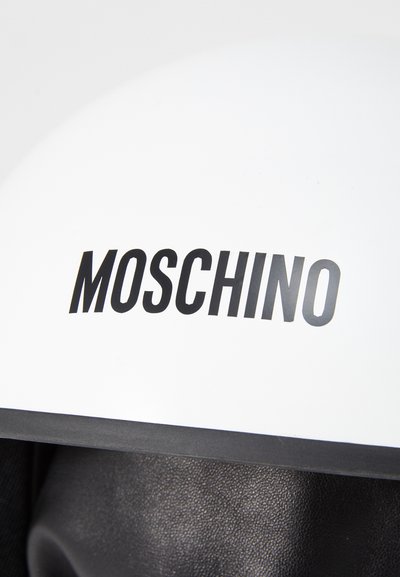 Hvid hjelm med mat finish, der har et fremtrædende sort "MOSCHINO" logo foran og en sort kant i bunden.