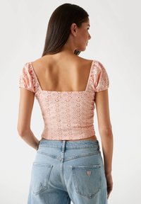 Top rosa pallido con maniche a sbuffo, scollatura quadrata e motivo fiorito a occhiello. Abbinato a jeans azzurri a vita alta.