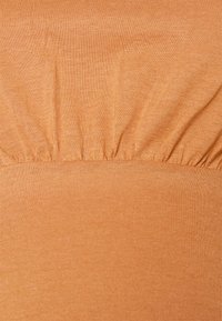 Close-up de um tecido laranja estriado com detalhe de costura franzida ao centro, mostrando a textura e a elasticidade do material.