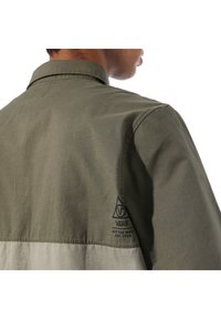 Groene en beige tweekleurige blouse met een kraag, voorzien van een logo op de mouw, vervaardigd uit een zachte katoenstof.