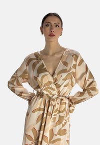 Robe portefeuille en tissu léger pêche avec des motifs floraux abstraits dans des tons beige et rouge. Elle possède des manches longues et une ceinture à nouer à la taille.