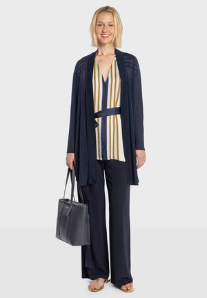 Cárdigan azul marino sobre una blusa de rayas con tonos dorados y blancos, combinado con pantalones oscuros y sandalias doradas. Incluye un bolso tote gris estructurado.