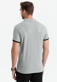 Šedé polo tričko s černým lemem na rukávech, vyrobené z měkkého materiálu. Má klasický límec a přiléhavý střih.