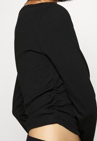 Černý dlouhý rukáv top z jemně žebrované látky, s kulatým výstřihem a na bocích s nařasenými detaily pro zvýšení textury.