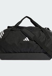Bolsa negra tipo duffle con correa ajustable para el hombro, que presenta acentos blancos de tres rayas, tela resistente y una base estructurada para dar soporte.