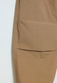 Bruine katoenstof met een gladde textuur, voorzien van een grote voorzak en keurig gestikte naden, gepresenteerd in een minimalistisch ontwerp.
