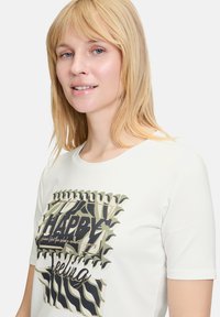 Witte katoenen t-shirt met een grafisch ontwerp met het woord "HAPPY" in het zwart, omringd door abstracte vormen in groen en zwart.