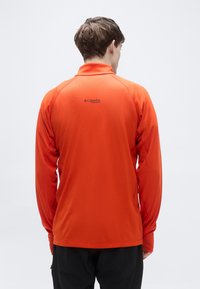 Πορτοκαλί μακρυμάνικο πουκάμισο με γιακά, υφασμάτινη υφή, με μαύρη επιγραφή "Columbia Titanium" στο πάνω μέρος της πλάτης.