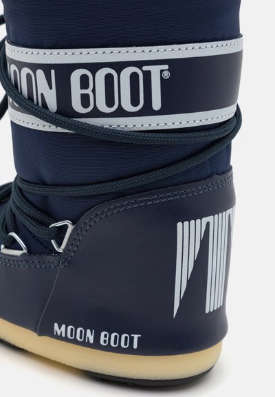 Námornícky modré Moon Boot s textúrovaným vonkajším povrchom, striebornými akcentmi a výrazným logom. Detail šnurovania s gumovou podrážkou a okrúhlym tvarom.
