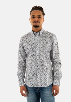 Chemise à manches longues boutonnière blanche, ornée d'un motif floral bleu et rouge. Tissu doux avec un col classique. Associée à un jean bleu.