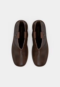 Par klasičnih tamnosmeđih kožnih cipela na slip-on, s zaobljenim četvrtastim prstima, gornjim trakama i vidljivim šavovima na bijeloj pozadini.