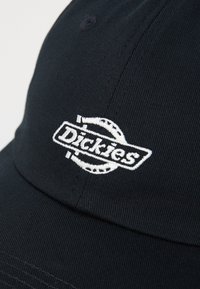 Cappello nero realizzato in tessuto testurizzato con logo "Dickies" ricamato bianco. Presenta una visiera curva e dettagli cuciti.