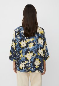 Blusa floral en azul, amarillo y negro con corte holgado y mangas de tres cuartos. Presenta una combinación de patrones de flores grandes y pequeñas.