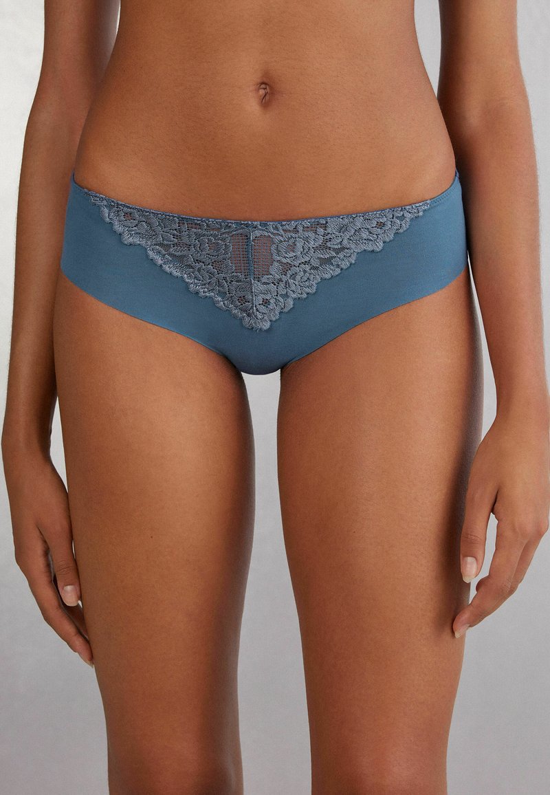 Ljusblå bikini-underkläder med intrikata spetsdetaljer längs midjan, med en mjuk tygkropp och en måttlig höjd.