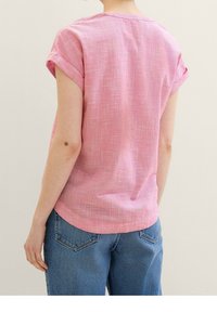 Kort lyserød kortærmet skjorte med et struktureret mønster, let buet kant og oprullede ærmer, parret med blå jeans.