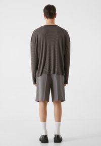 Chemise à manches longues rayée gris foncé à coupe décontractée, associée à un short gris. Des chaussures noires et des chaussettes blanches complètent le look.