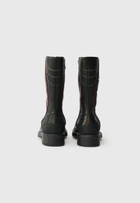 Svarte lær ankelsko med tekstur, kontrasterende maroon siden, stablet hæl og dekorativ søm. Glidelås lukking på siden.