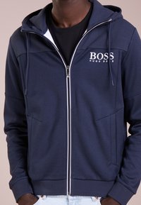 Marinblå zip-up hoodie med texturerade övre paneler, framfickor och vita dragkedjedetaljer. Har 'BOSS'-logotypen på vänster bröst.