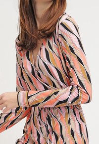 Robe colorée présentant un motif avec des rayures ondulées en rose, orange, noir et beige. Manches longues et décolleté en V pour un attrait supplémentaire.