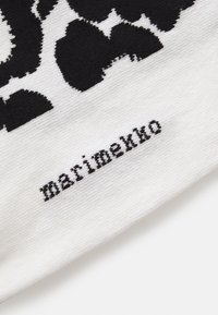 Tejido blanco con un gran patrón floral negro y la palabra "marimekko" bordada en hilo negro en la esquina inferior derecha.