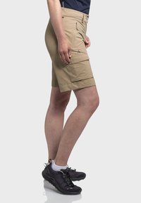 Beige Cargo-Shorts mit mehreren Taschen, einem Bund mit Knopf und geradem Schnitt. Getragen mit schwarzen Sportschuhen und weißen Socken.