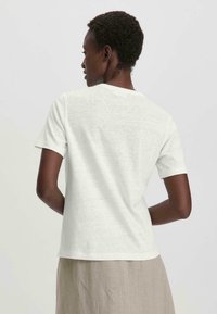 T-shirt blanc à manches courtes en coton avec un col rond, présenté de dos. Texture lisse avec un design minimaliste.