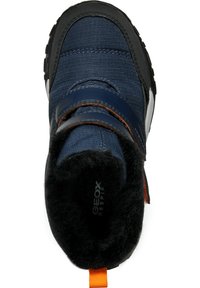 Zapatilla de deporte azul marino con parte superior de textil y suela de goma negra. Cuenta con una correa de Velcro, un forro interior de felpa y una lengüeta de tirón naranja.