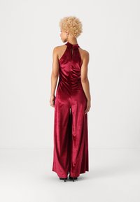 Samaninės bordo spalvos šokinėjimas su aukštu apykakle, atvira nugarine ir plačiomis kojomis, pasižymintis elegantišku dizainu ir subtiliu blizgesiu.